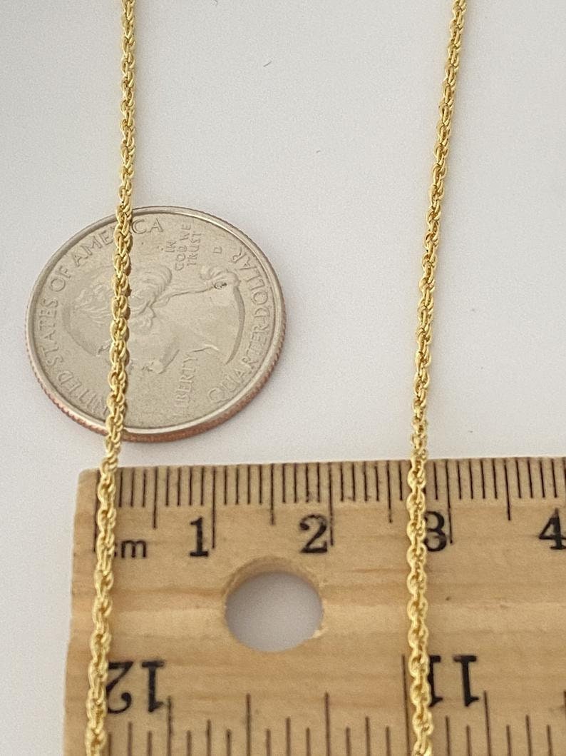 Puede incluir: Un collar de cadena de cuerda dorada que mide 45,7 cm de largo. La cadena se muestra junto a una regla y una moneda de veinticinco centavos de d&oacute;lar estadounidense para referencia de tama&ntilde;o.