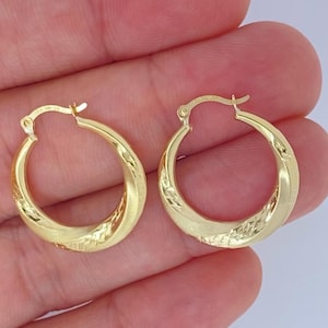May include: A pair of gold hoop earrings. Each earring has a rounded shape with a textured, diamond-like pattern on the lower half. The earrings are held in a hand against a light background.