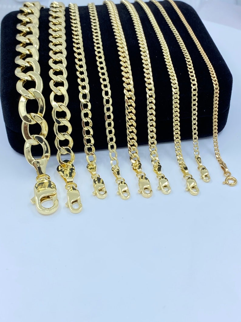 May include: A set of eight gold chains of varying widths and lengths, displayed on a black velvet background. The chains are all made of a classic curb link style.