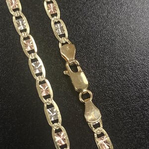 May include: Gold-tone necklace with a unique design. The chain features alternating oval links with a three-tone starburst pattern. The clasp is also gold-toned. The necklace is displayed on a dark surface.