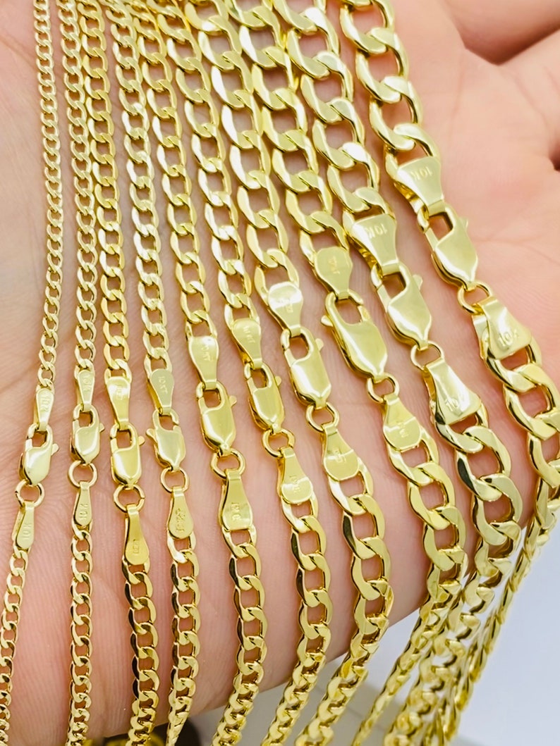 May include: A set of ten gold chains of varying widths and lengths. The chains are arranged in a fan shape, with the widest chain at the top and the narrowest chain at the bottom.