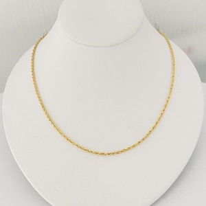 Puede incluir: Un collar de cadena de cuerda dorada en un expositor blanco.