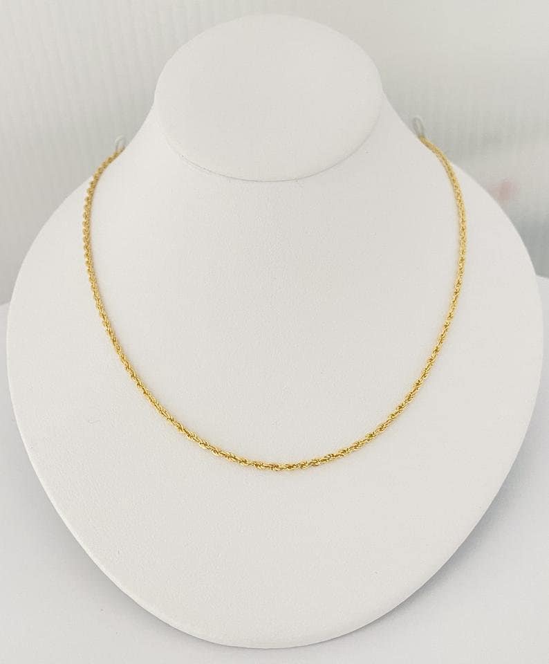 Puede incluir: Un collar de cadena de cuerda dorada en un expositor blanco.