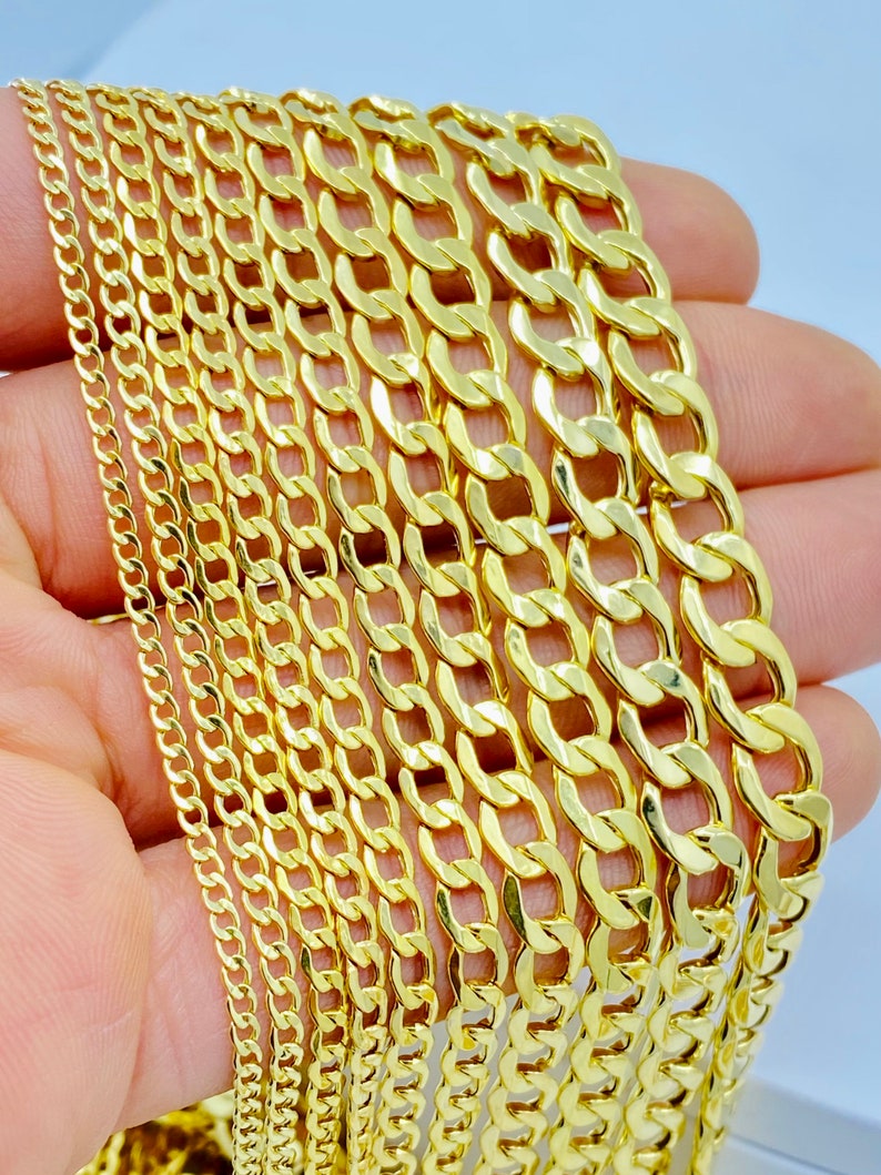 May include: A collection of gold curb chains of varying widths. The chains are arranged in a stack, with the widest chain at the bottom and the narrowest chain at the top.