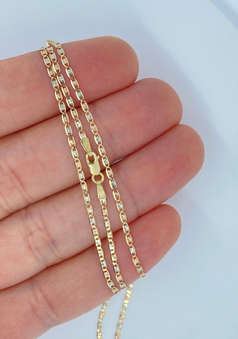 K&ouml;nnte beinhalten: Eine goldene Kettenkette mit dreifarbigem Design. Die Kette besteht aus Gelb-, Wei&szlig;- und Ros&eacute;gold. Die Kette liegt auf einer Hand.