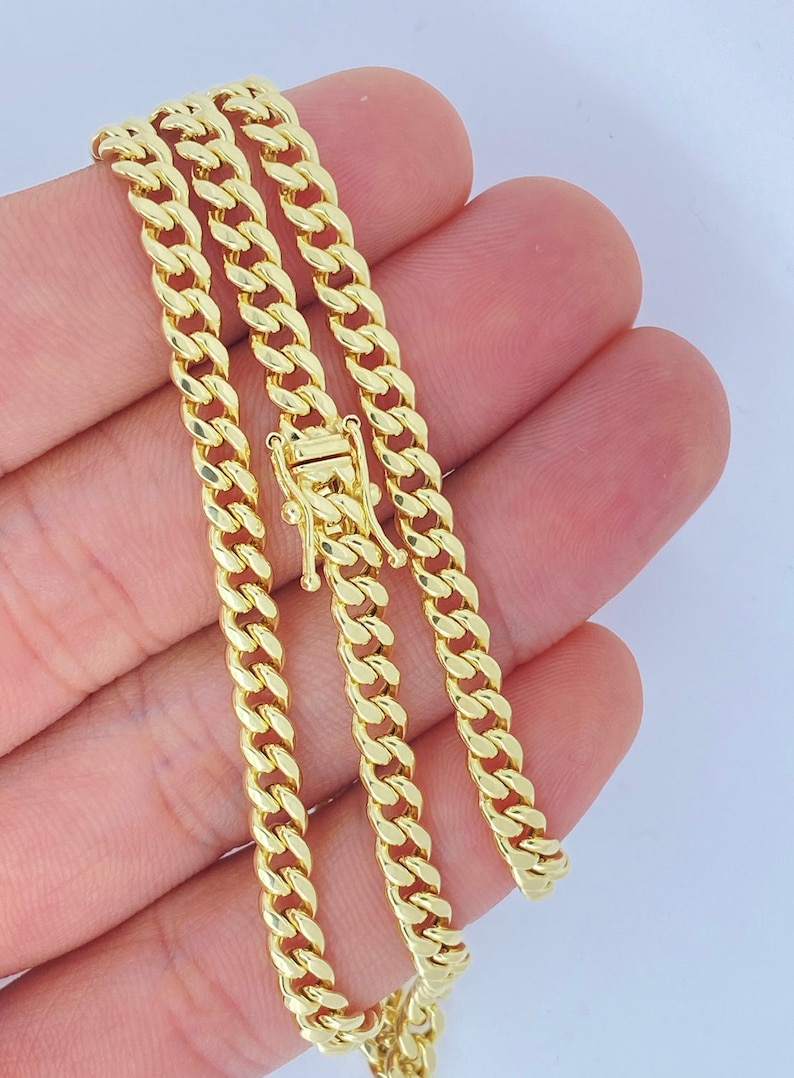 May include: A gold curb chain necklace with a lobster clasp closure. The chain is folded in thirds, showing the length and width of the chain links.