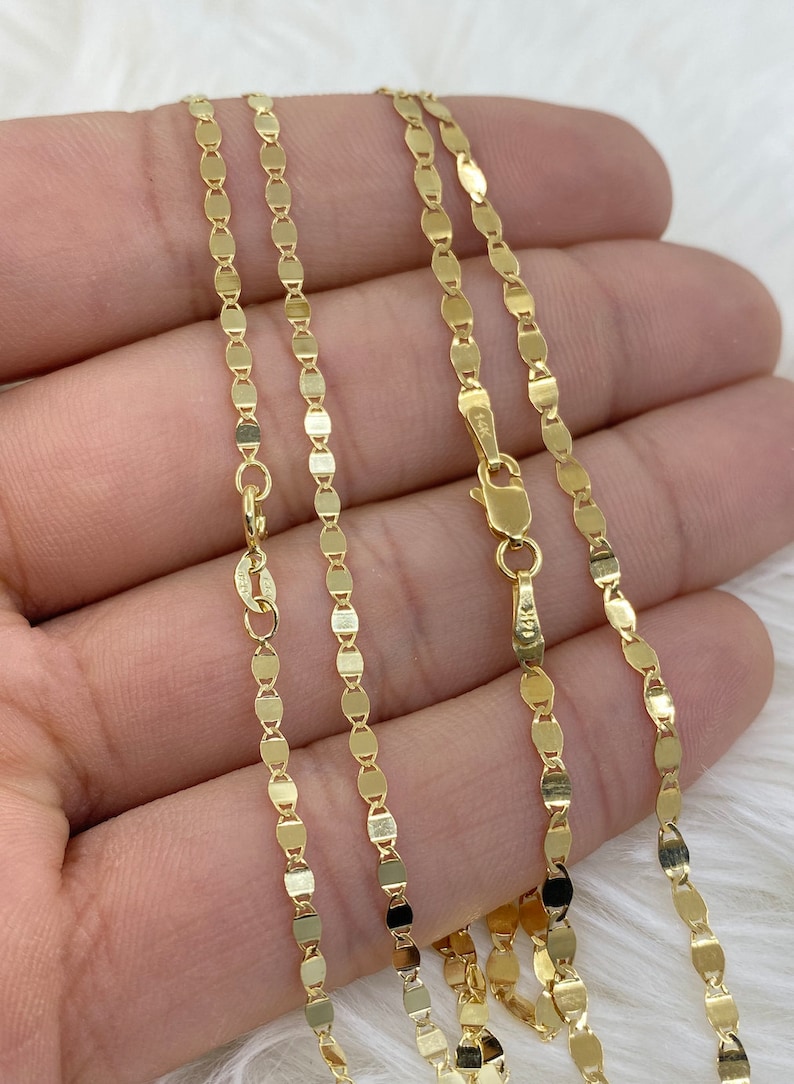 May include: A gold chain necklace with a delicate, oval-shaped link pattern. The chain is shown on a hand, with the clasp visible.