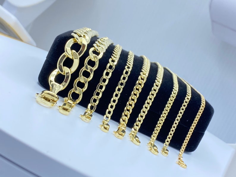 May include: A set of eight gold chains of varying widths and lengths displayed on a black velvet background. The chains are arranged in order of size, with the largest chain at the top and the smallest chain at the bottom.