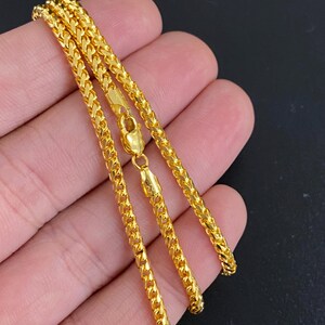 May include: A gold chain necklace with a classic Franco chain design. The chain is shown folded in half on a hand.