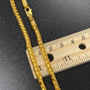 May include: A gold chain necklace with a lobster clasp. The chain is measured against a ruler, showing it is approximately 5 cm long.
