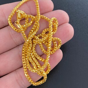May include: A gold chain necklace with a delicate, intricate design. The chain is made of small, linked squares that create a textured look.