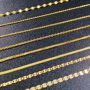 May include: A selection of gold necklaces featuring various chain designs, including beaded, cable, and flat styles. The chains are displayed on a dark surface, highlighting their golden colour and intricate details. The image shows a variety of necklace styles.