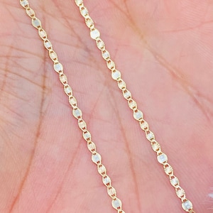 May include: A gold chain necklace with a delicate, patterned design. The chain is made of small, oval-shaped links.
