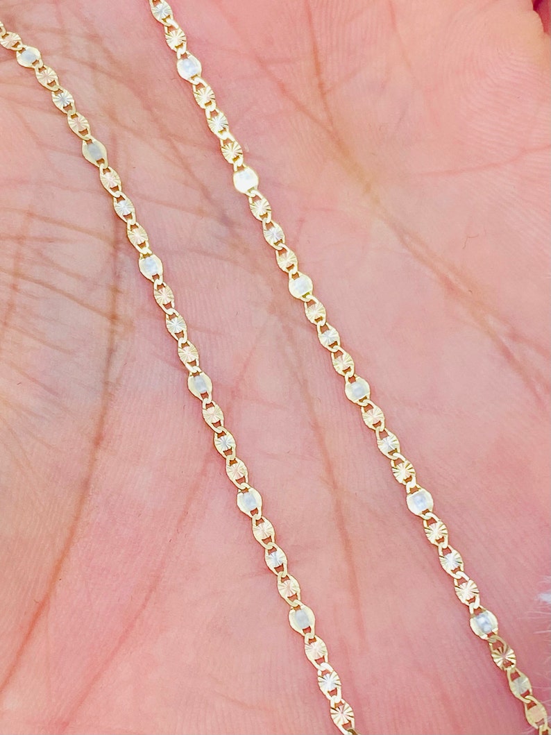 May include: A gold chain necklace with a delicate, patterned design. The chain is made of small, oval-shaped links.