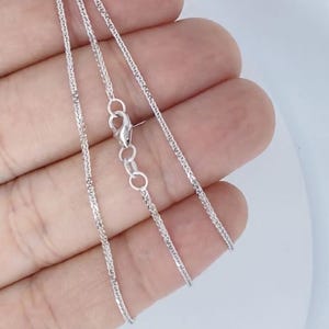 May include: A silver chain necklace with a lobster clasp. The chain is a delicate, braided design.