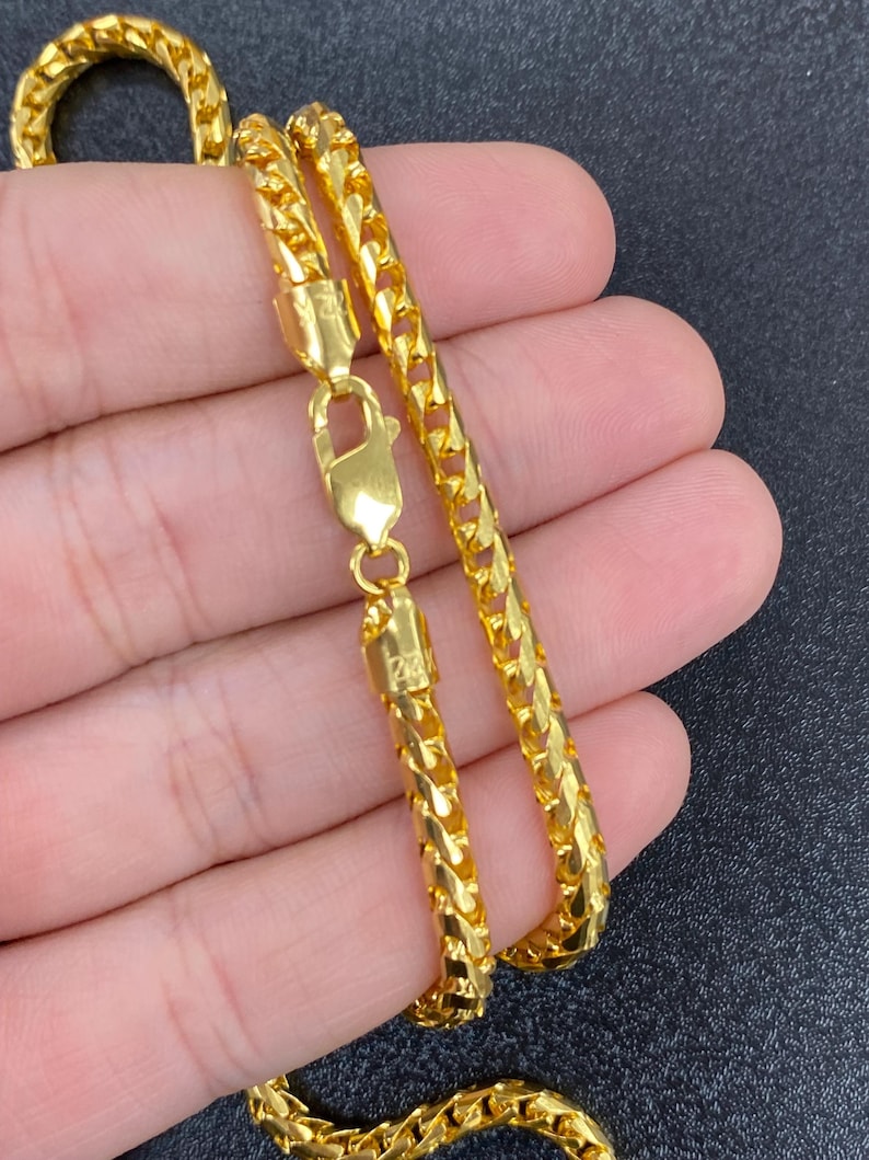 May include: A gold chain necklace with a lobster clasp. The chain is a Franco chain style, which is a flat, woven chain.