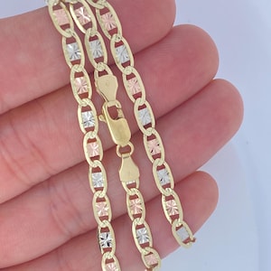 May include: A gold-toned chain necklace with alternating oval links and decorative accents in gold, rose gold, and silver. The necklace features a lobster clasp closure. The jewelry is displayed against a light background.