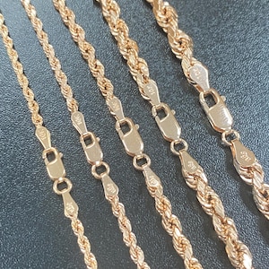 May include: Close-up of several gold rope chains with clasps. The chains vary in thickness and are displayed against a dark background. The clasps are marked with "10K" and "a2g" stamps.