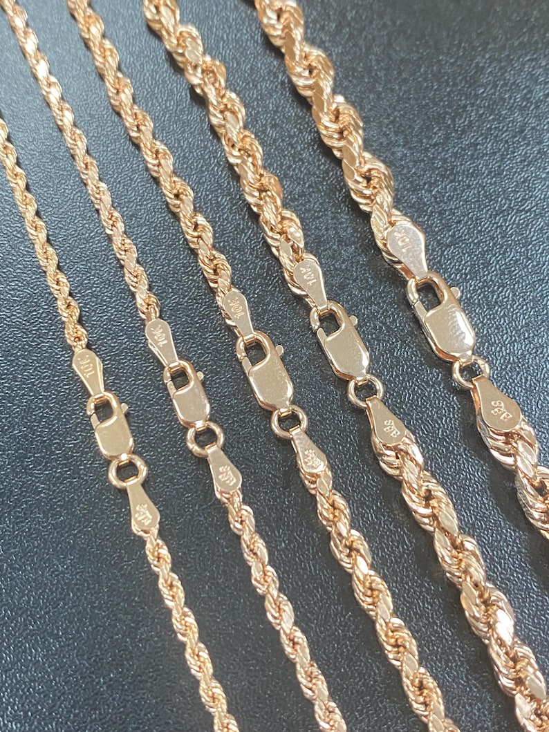 May include: Close-up of several gold rope chains with clasps. The chains vary in thickness and are displayed against a dark background. The clasps are marked with "10K" and "a2g" stamps.