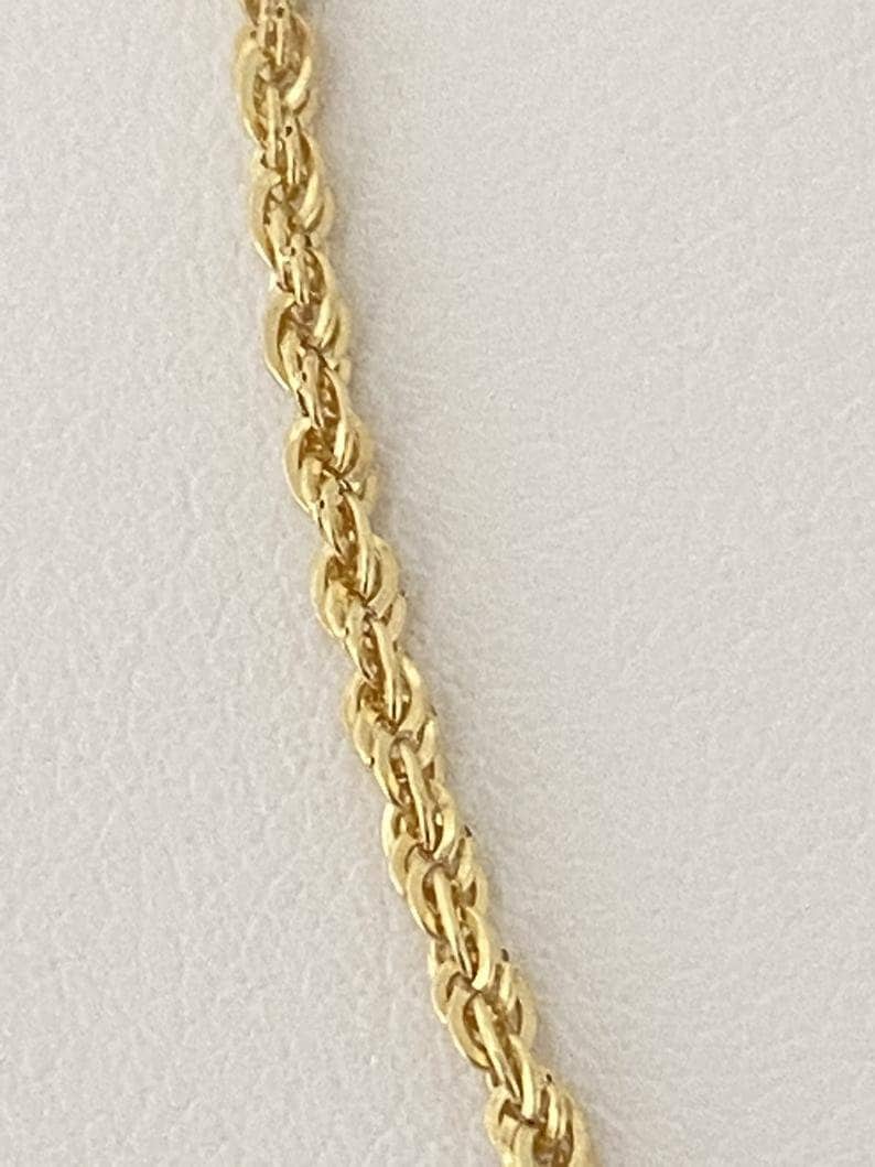 Puede incluir: Primer plano de un collar de cadena de cuerda dorada. La cadena est&aacute; hecha de peque&ntilde;os eslabones interconectados que forman un patr&oacute;n de cuerda.