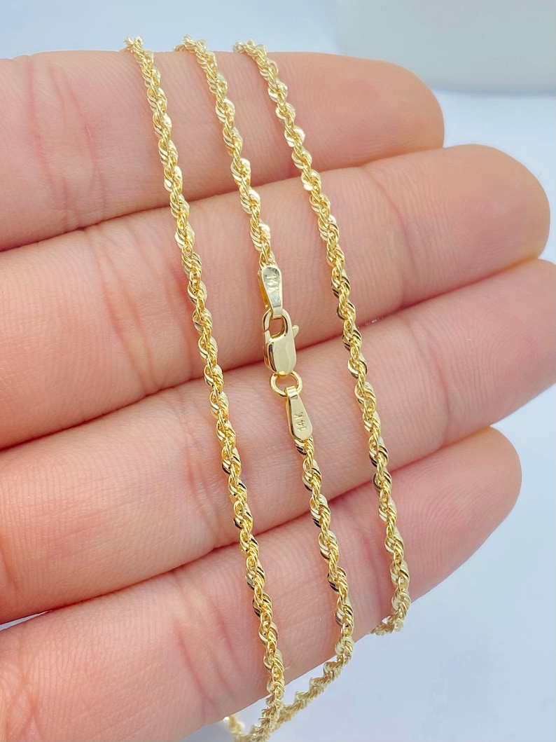 Puede incluir: Un collar de cadena de cuerda de oro con un cierre de langosta. La cadena se muestra en una mano.