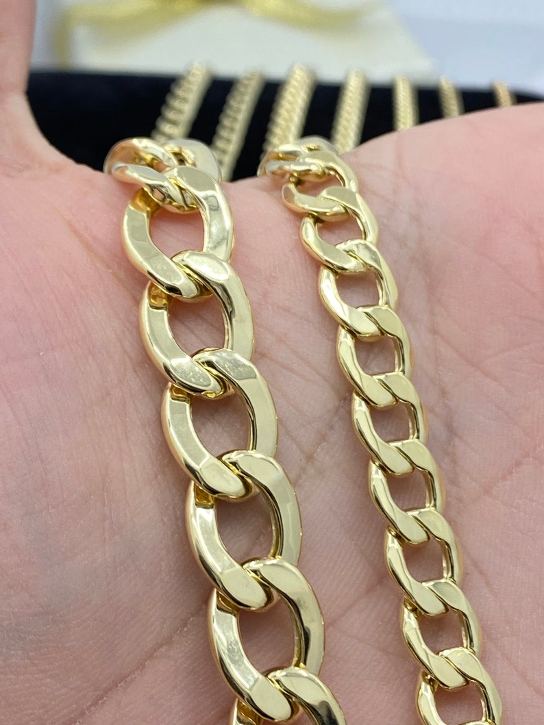May include: Two gold chains, one thicker than the other, are shown on a hand. Both chains are made of a classic curb link style.