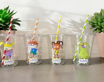 May include: Four clear plastic cups with colorful straws and cartoon character stickers. Each cup has a different character from the Rugrats cartoon. The characters are Tommy Pickles, Chuckie Finster, Angelica Pickles, and Reptar.