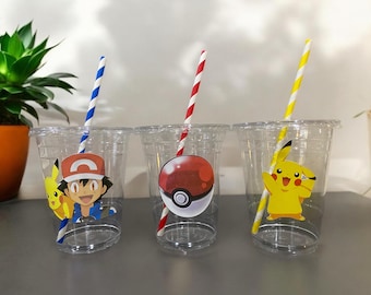 May include: Three clear plastic cups with colorful straws and Pokemon-themed decorations. One cup features Ash Ketchum, another a Poke Ball, and the third Pikachu. Each cup has a different striped straw.