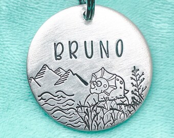 May include: Silver dog tag with a mountain range, a dinosaur, and the name "BRUNO" engraved on it.