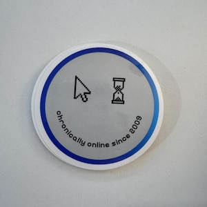 Puede incluir: Una pegatina redonda con un borde azul y un fondo gris. La pegatina presenta un cursor de ratón de computadora y un reloj de arena, con el texto "chronically online since 2009".