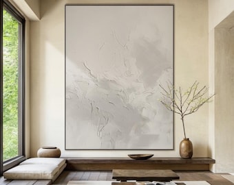May include: A large abstract painting in shades of white and gray hangs on a wall in a minimalist living room. The painting has a textured surface and features swirling, organic shapes. The room is decorated with a wooden coffee table, a small plant, and a cushion on the floor.