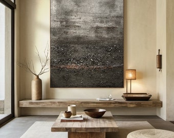 May include: A large abstract painting in shades of gray and brown hangs on a wall in a modern living room. The painting features a textured surface and a horizontal line of rust-colored paint. The painting is displayed above a wooden shelf and a coffee table.