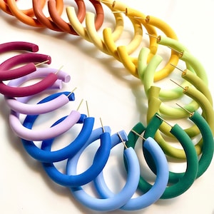 May include: A set of colourful hoop earrings in various shades of blue, green, purple, yellow, and red. The earrings are made of a thick, rounded material and have a gold-toned post.