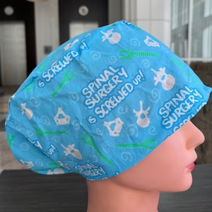 May include: A blue surgical scrub hat with a white and green print. The print features the text "Spinal Surgery is Screwed Up!" and a stylised image of a human spine.