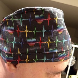 Peut inclure: Un bonnet de travail noir avec un cœur arc-en-ciel et un motif d'ECG.