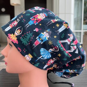 May include: A black scrub hat with a colourful pattern of nutcrackers and ballerinas. The pattern is repeated throughout the hat.