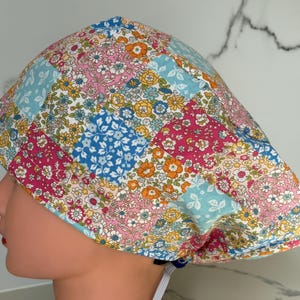 May include: A colorful patchwork scrub cap featuring a floral pattern in shades of pink, blue, yellow, and orange. The cap is designed with a comfortable fit and includes an adjustable tie for a secure wear.