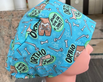 May include: Blue surgical scrub hat with a white drawstring. The hat has a repeating pattern of bones, stars, and text that says "Ortho", "Always time for a joint!" and "We do joints!"