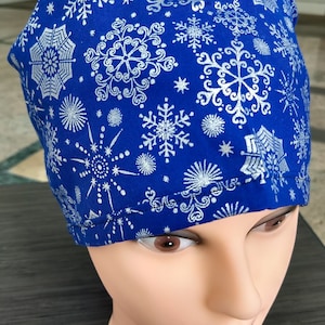 Può includere: Un berretto chirurgico blu con un motivo a fiocco di neve bianco.