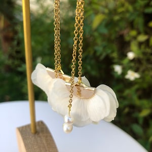 Puede incluir: Un par de pendientes de cadena dorada con abalorios en forma de flor blanca y detalles de perlas.