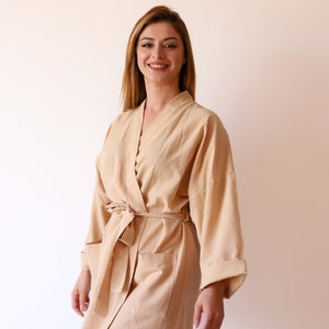 Könnte beinhalten: Ein hellbraunes Gewand mit langen Ärmeln und einem Bindegürtel. Das Gewand hat eine Tasche auf der linken Seite.