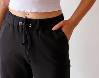 Puede incluir: Pantalón negro con cintura de cordón y ojales dorados. El pantalón tiene un corte holgado y está hecho de una tela suave y cómoda.