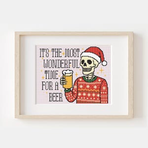 May include: A framed cross-stitch featuring a skeleton wearing a Santa hat and a Christmas sweater, holding a beer. The text reads "IT'S THE MOST WONDERFUL TIME FOR A BEER" in a festive font, with star accents.