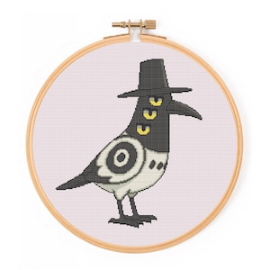 May include: Cross-stitch embroidery of a stylized crow wearing a black hat, with three yellow eyes and a long beak. The crow has a black and white body with a circular design on its chest. The embroidery is set in a wooden hoop.