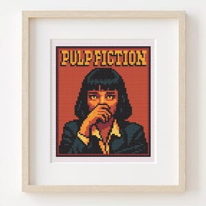 Può includere: Arte a punto croce incorniciato con un ritratto pixelato di una donna del film Pulp Fiction. L'opera d'arte ha uno sfondo rosso con le parole "PULP FICTION" in giallo e nero. La donna indossa una giacca nera.