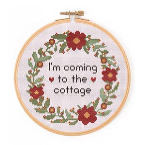 May include: A cross-stitch embroidery hoop with the text "I'm coming to the cottage" surrounded by a wreath of red flowers, green leaves, and berries. The embroidery is set in a wooden hoop.