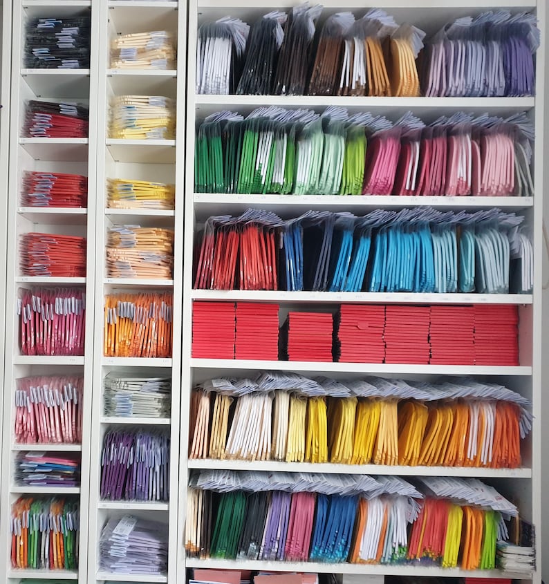 May include: A white shelf unit with multiple shelves filled with stacks of colorful fabric squares. The fabric squares are arranged in rows and columns, creating a visually appealing pattern.