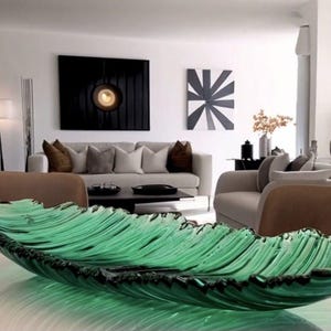 Puede incluir: Un plato de servir grande de vidrio verde con forma de hoja. El plato tiene una superficie texturizada y está sobre una mesa blanca.