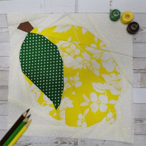 Puede incluir: Una tela amarilla con estampado floral blanco y tela de lunares verdes se corta en forma de pera. La tela está sobre un fondo blanco con un pequeño patrón de lunares blancos.