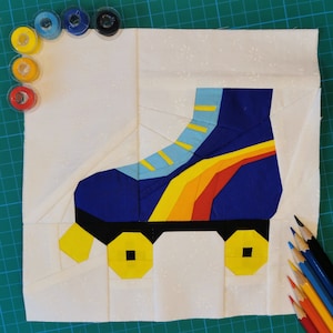 Könnte beinhalten: Ein weißer Stoffquadrat mit einem blauen, gelben und roten Rollschuh-Design. Der Rollschuh hat schwarze Räder und befindet sich auf einem weißen Hintergrund.